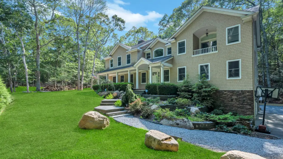 A large house with a covered porch stands beside a landscaped lawn.