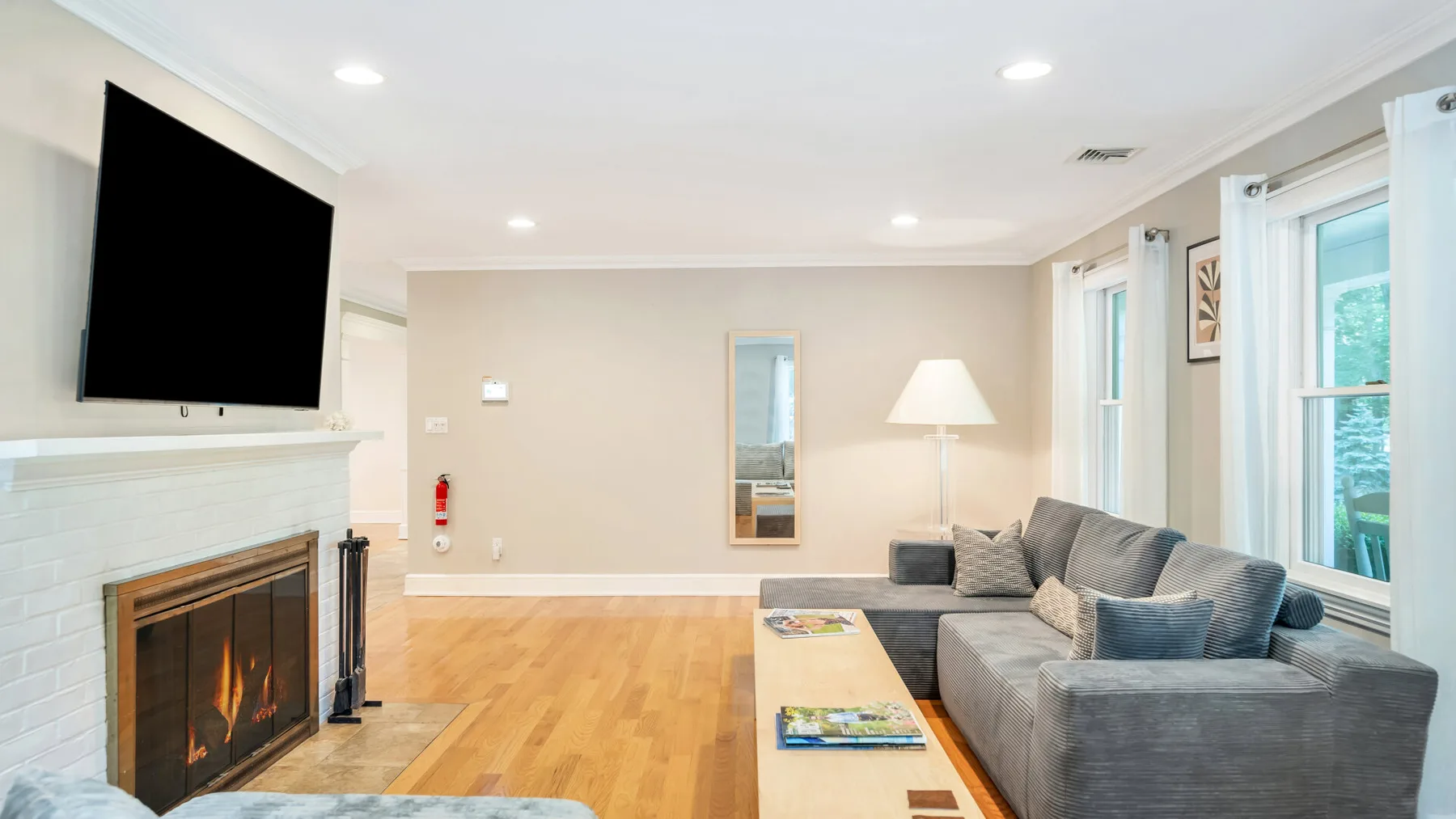 A bright living room with a gray sectional, fireplace, and television.