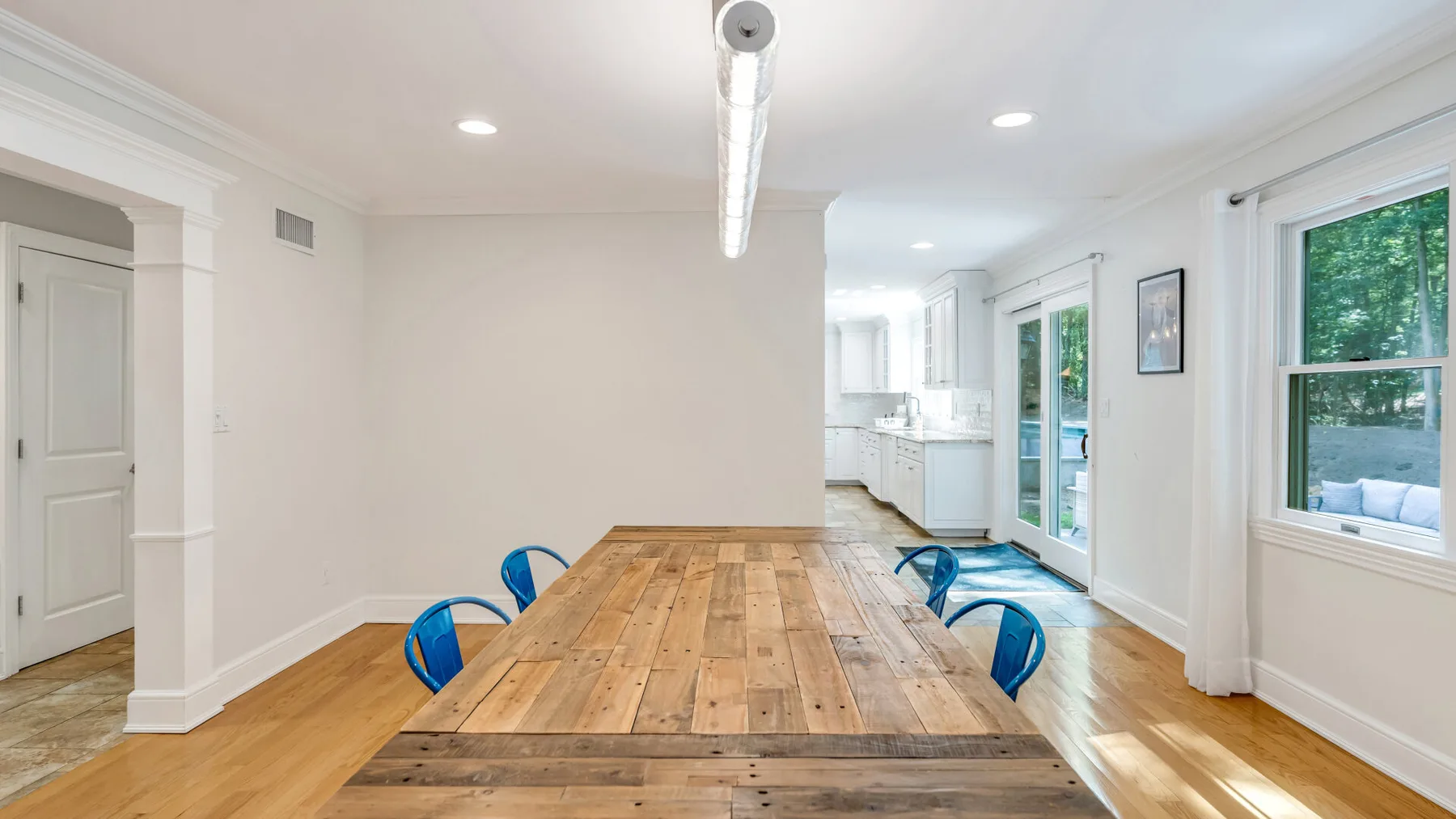 A bright dining area features a long wooden table and blue seating.