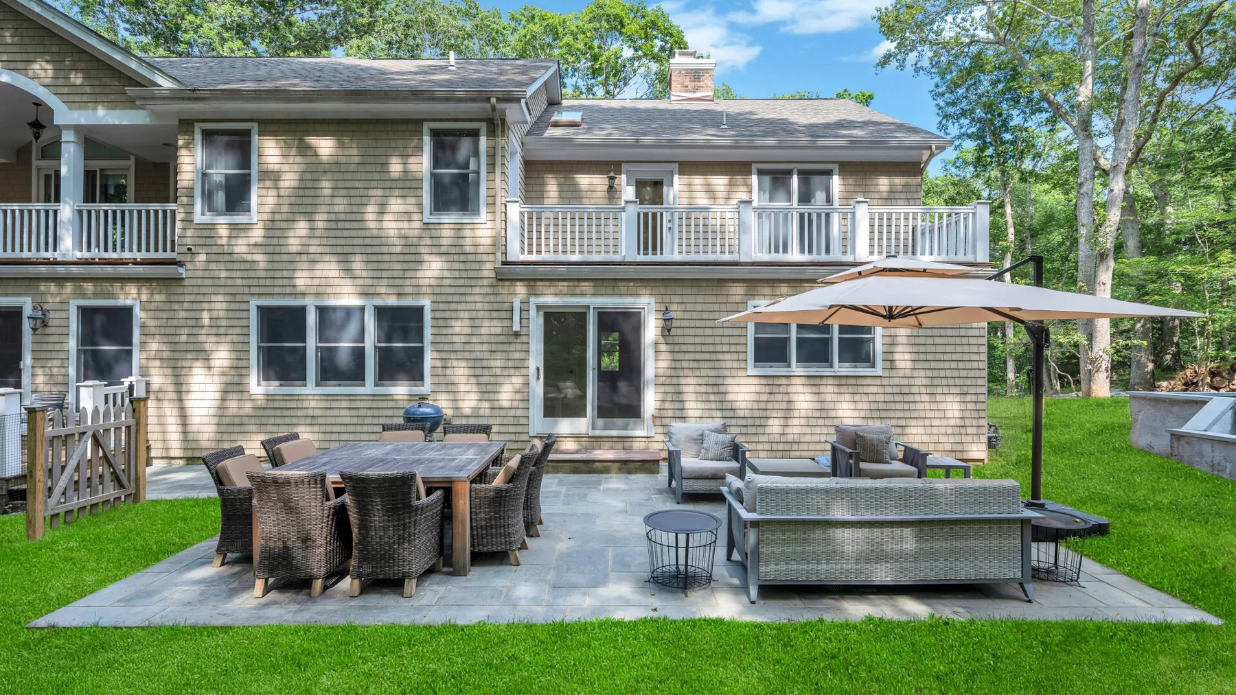 A house patio has outdoor dining and lounge seating beneath a large umbrella.