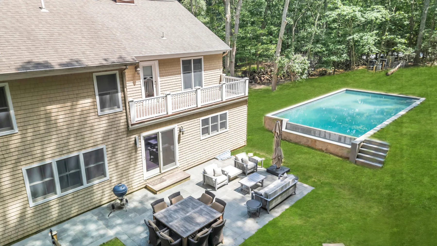 A house patio and raised swimming pool sit beside a green lawn.