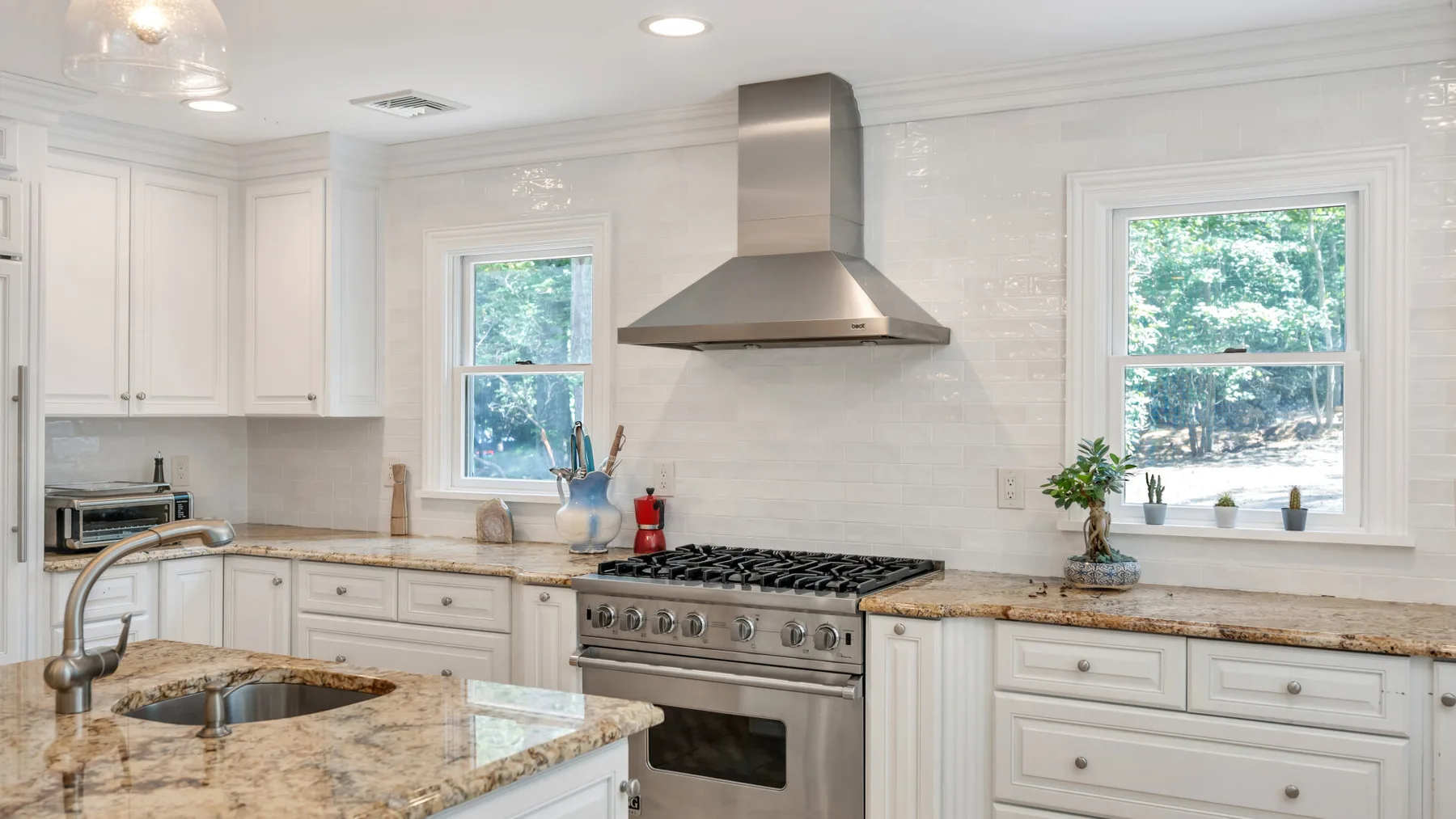 A bright kitchen with white cabinetry, a cooking range, and a stone island.