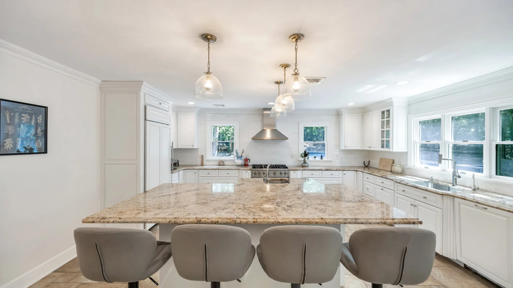 A bright kitchen with white cabinetry, a large island, and windows along the counter.