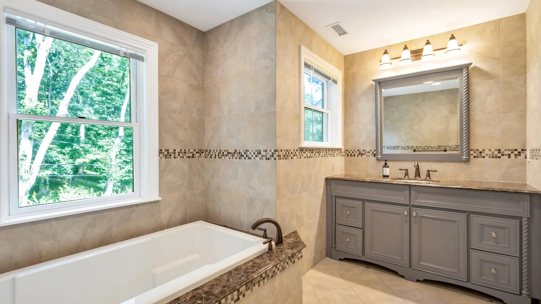 A bathroom with a bathtub, vanity, and window overlooking trees.