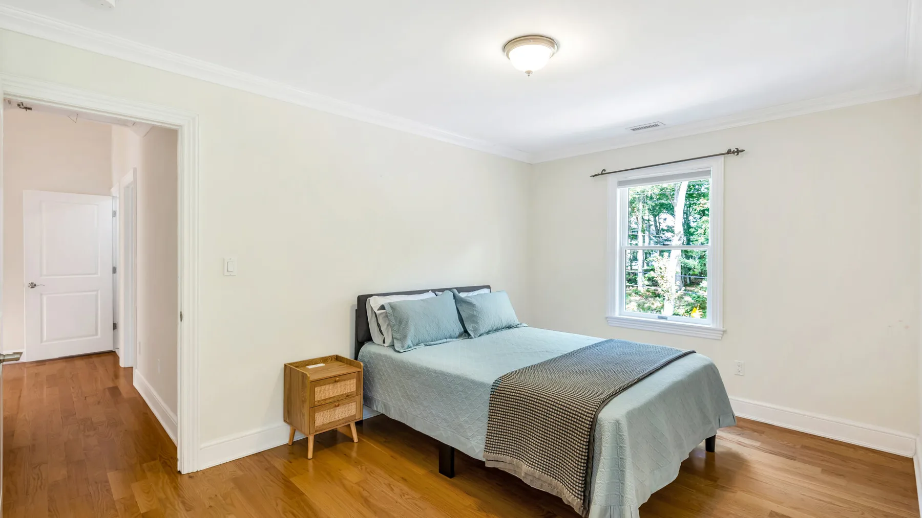 A bedroom with a bed and a window overlooking greenery.