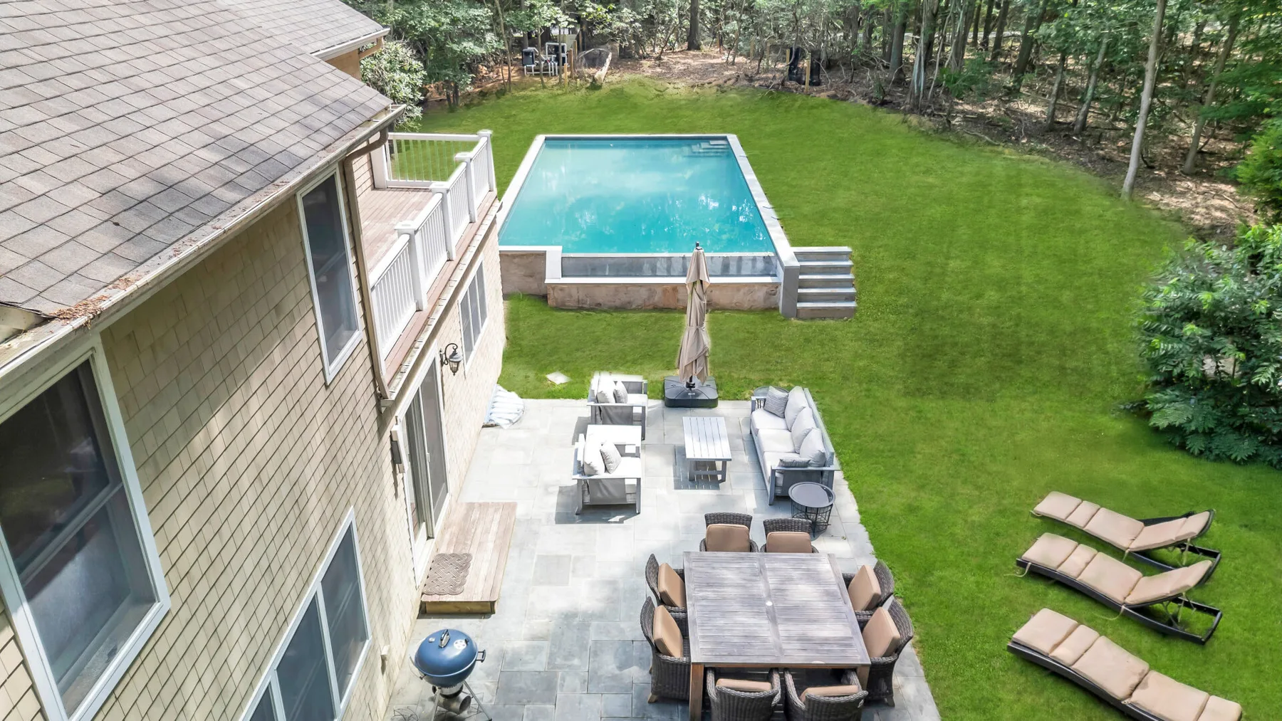A backyard patio with outdoor seating overlooks a swimming pool and lawn.