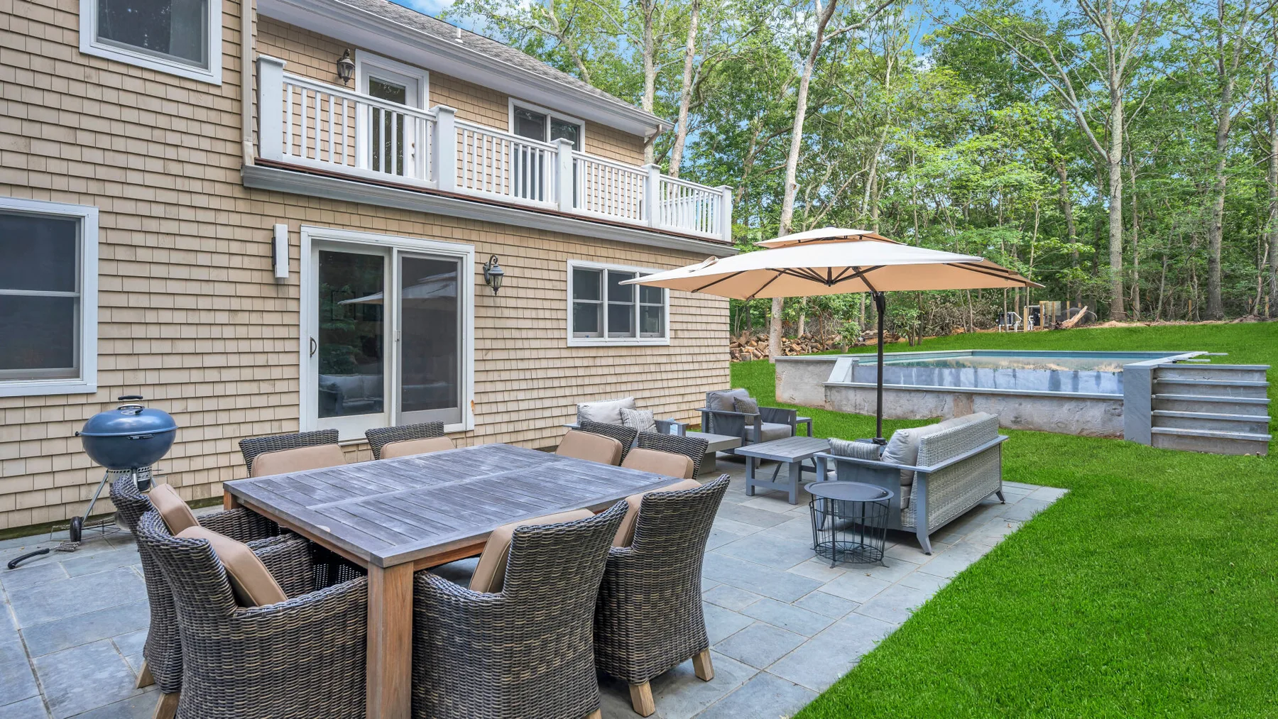 A patio seating area with a dining table and umbrella beside a house.