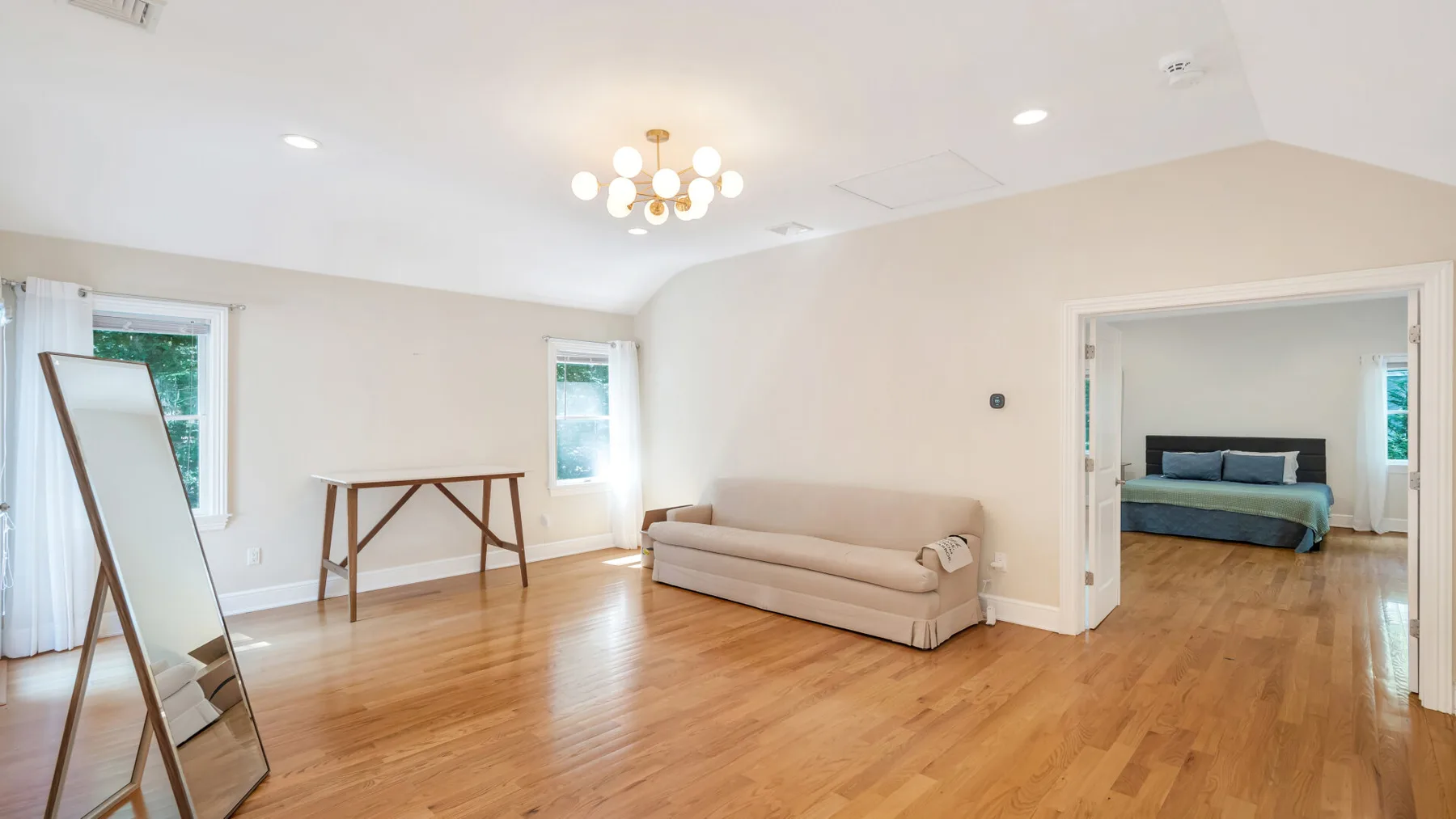 A bright living room with wood flooring, a sofa, and a doorway to a bedroom.