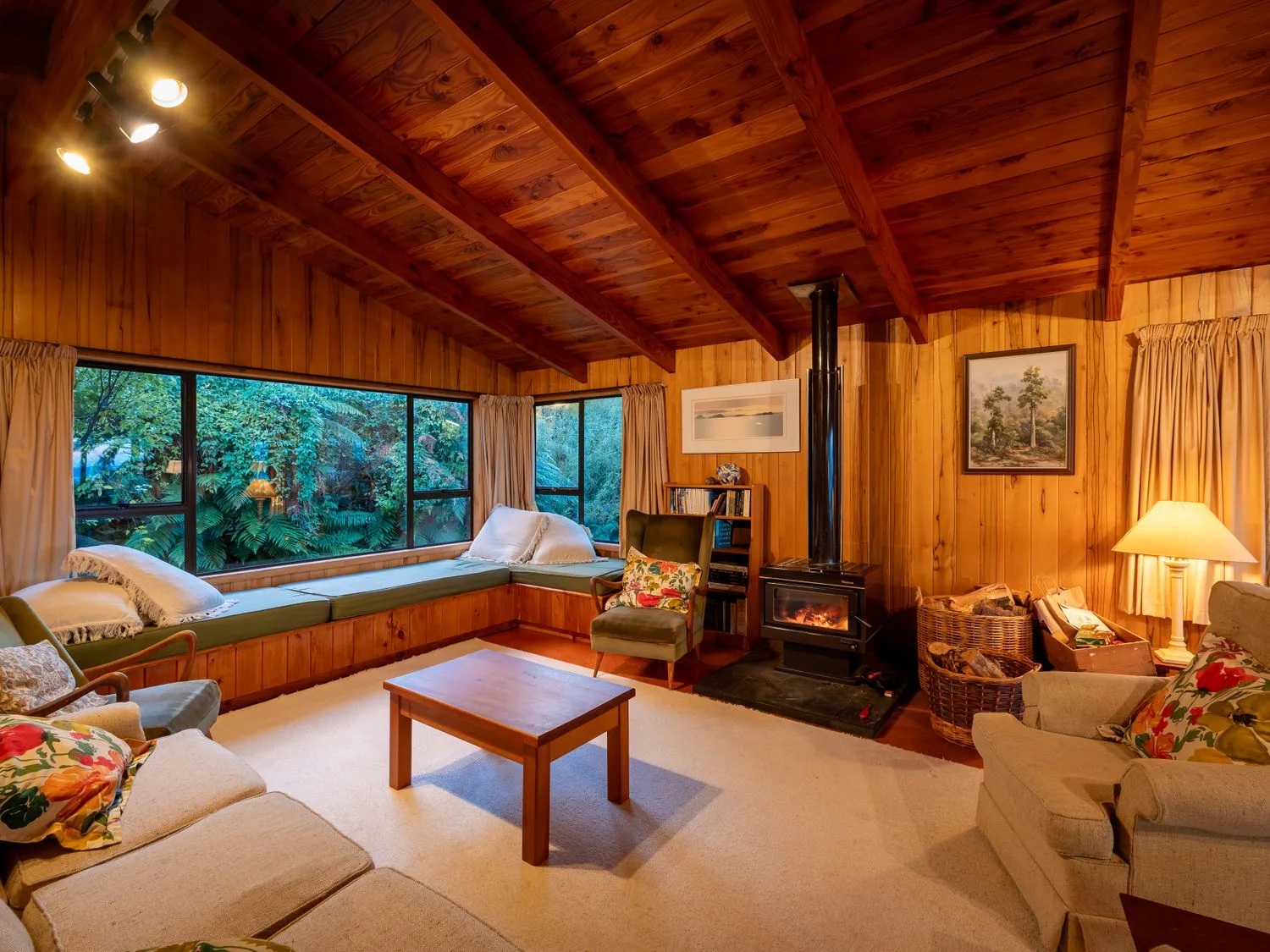A living room with wooden walls and ceiling a wood stove and a corner bench seating at Lake View Lodge - Taupo Holiday Home in Pukawa Bay