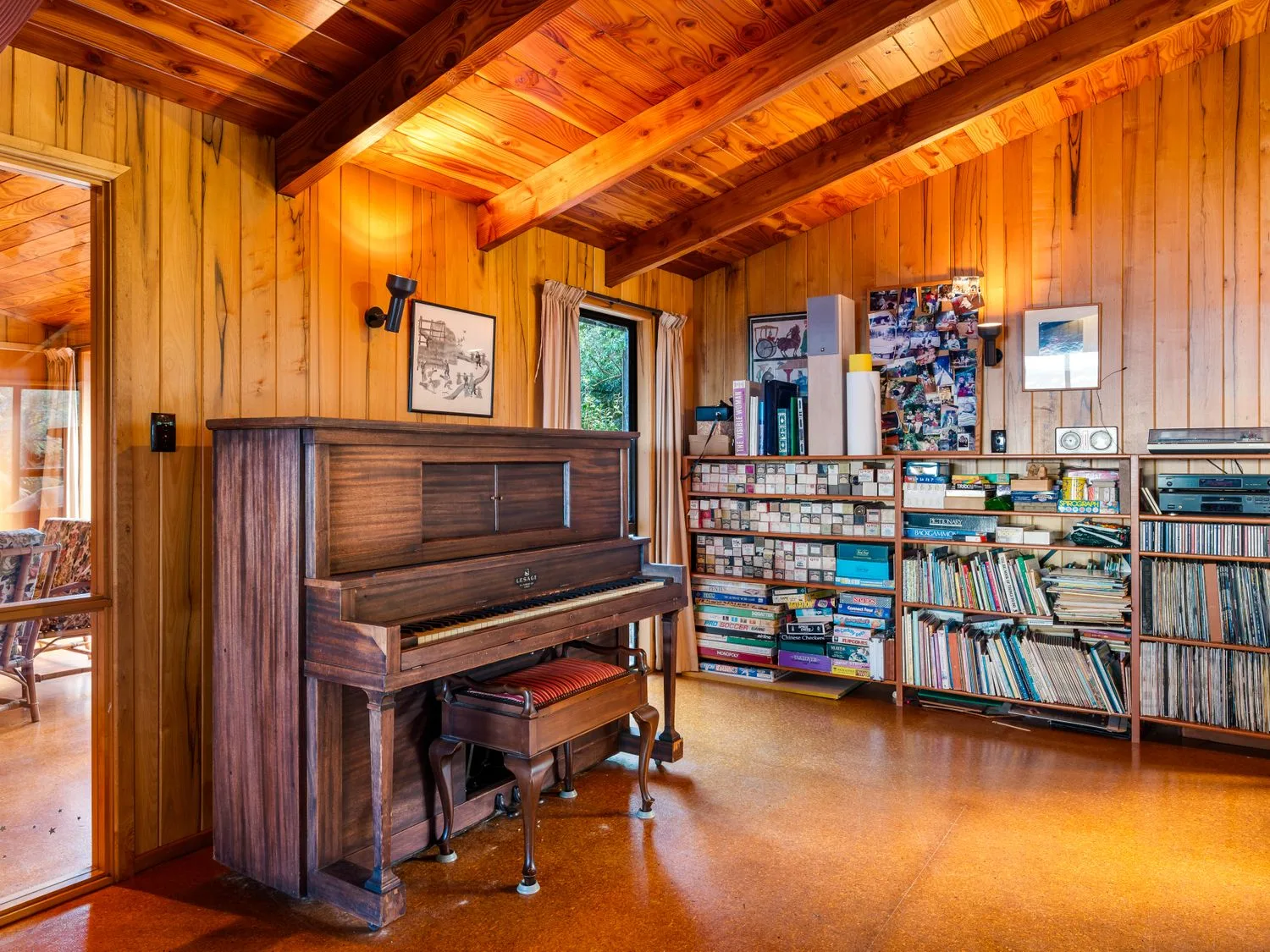 A wood-paneled room with an upright piano and shelves of books and records.