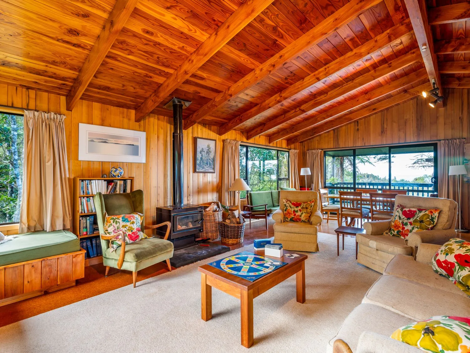 A wood-paneled living room with seating around a coffee table and windows overlooking the water.