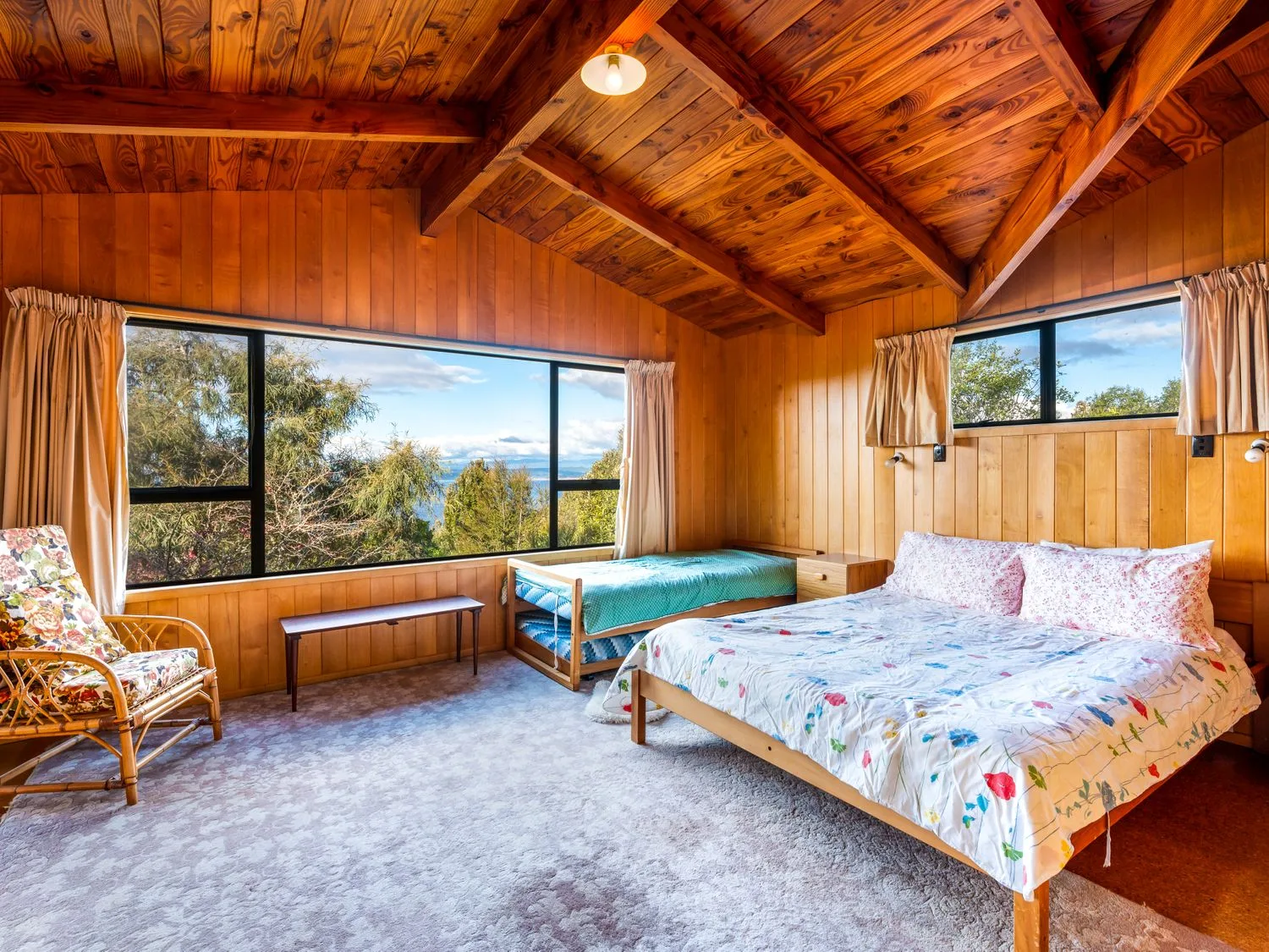 A wood-paneled bedroom with two beds and large windows overlooking trees.