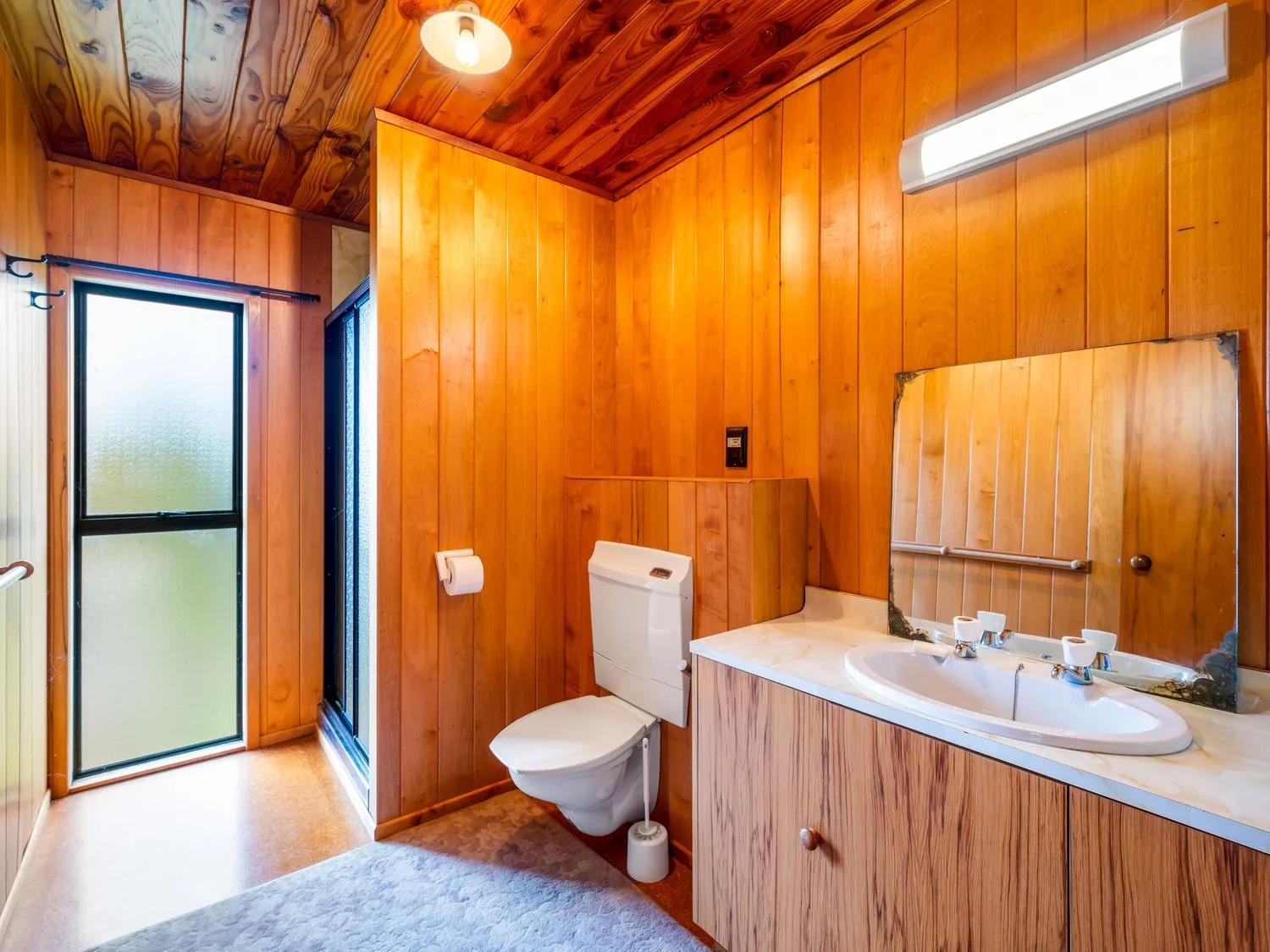 A bathroom with wood-paneled walls, a toilet, and a sink beneath a mirror.