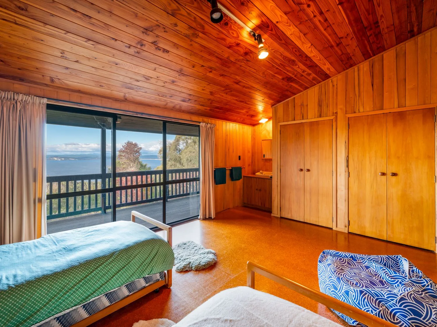A wood-paneled bedroom with beds and a sliding glass door opening onto a balcony.