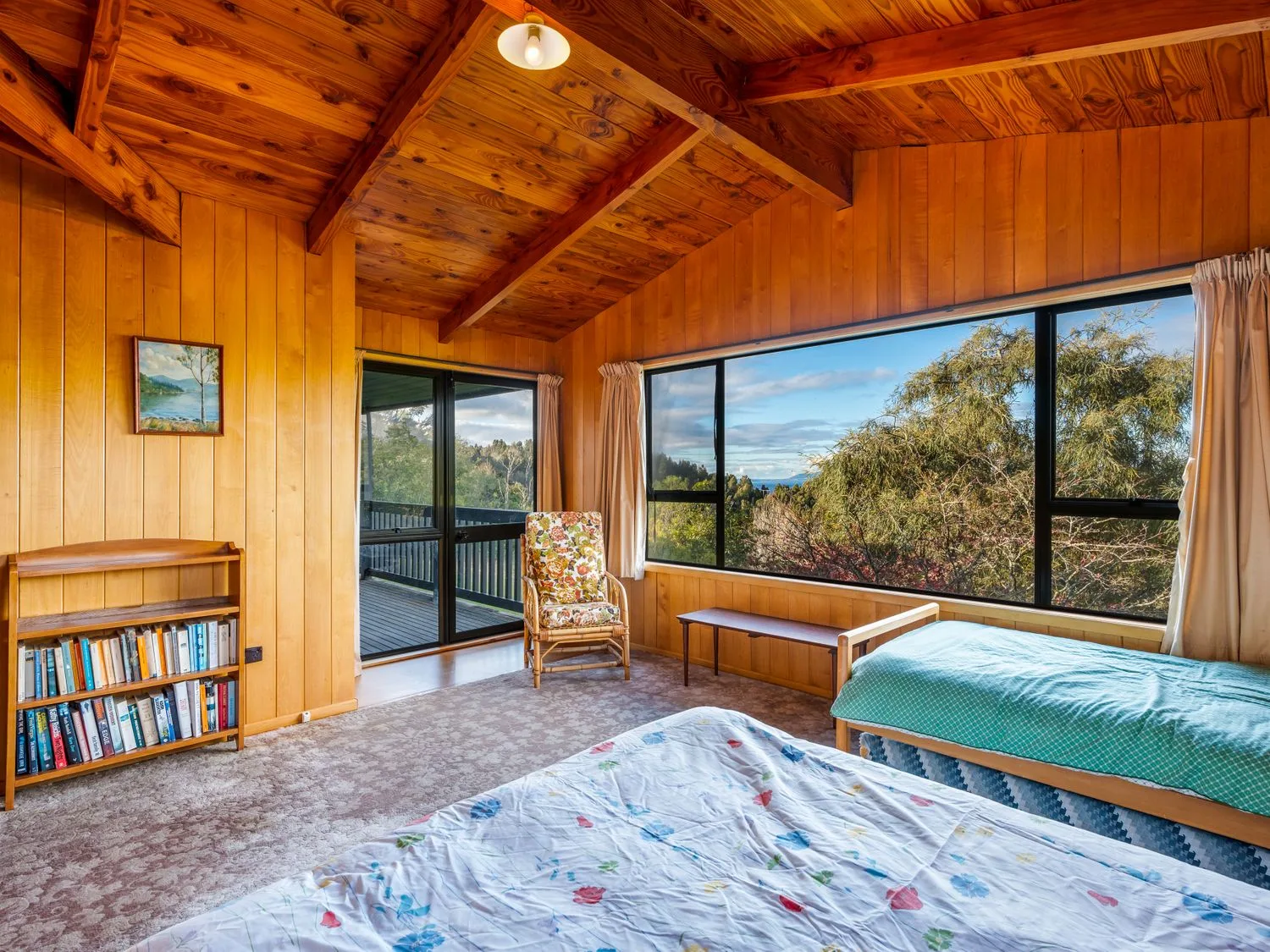 A wood-paneled bedroom with two beds and large windows overlooking trees.