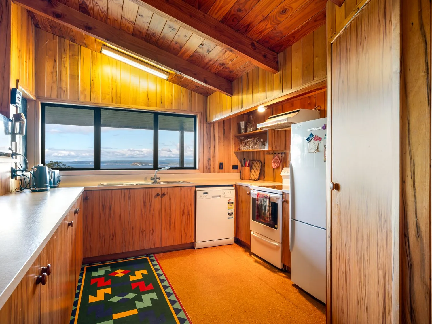 A kitchen with wooden cabinets, a refrigerator, a stove, and a colorful floor runner.