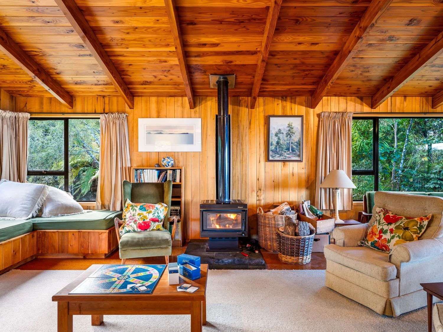 A living room with wooden walls and ceiling two armchairs a wood stove and a coffee table with a board game at Lake View Lodge - Taupo Holiday Home in Pukawa Bay