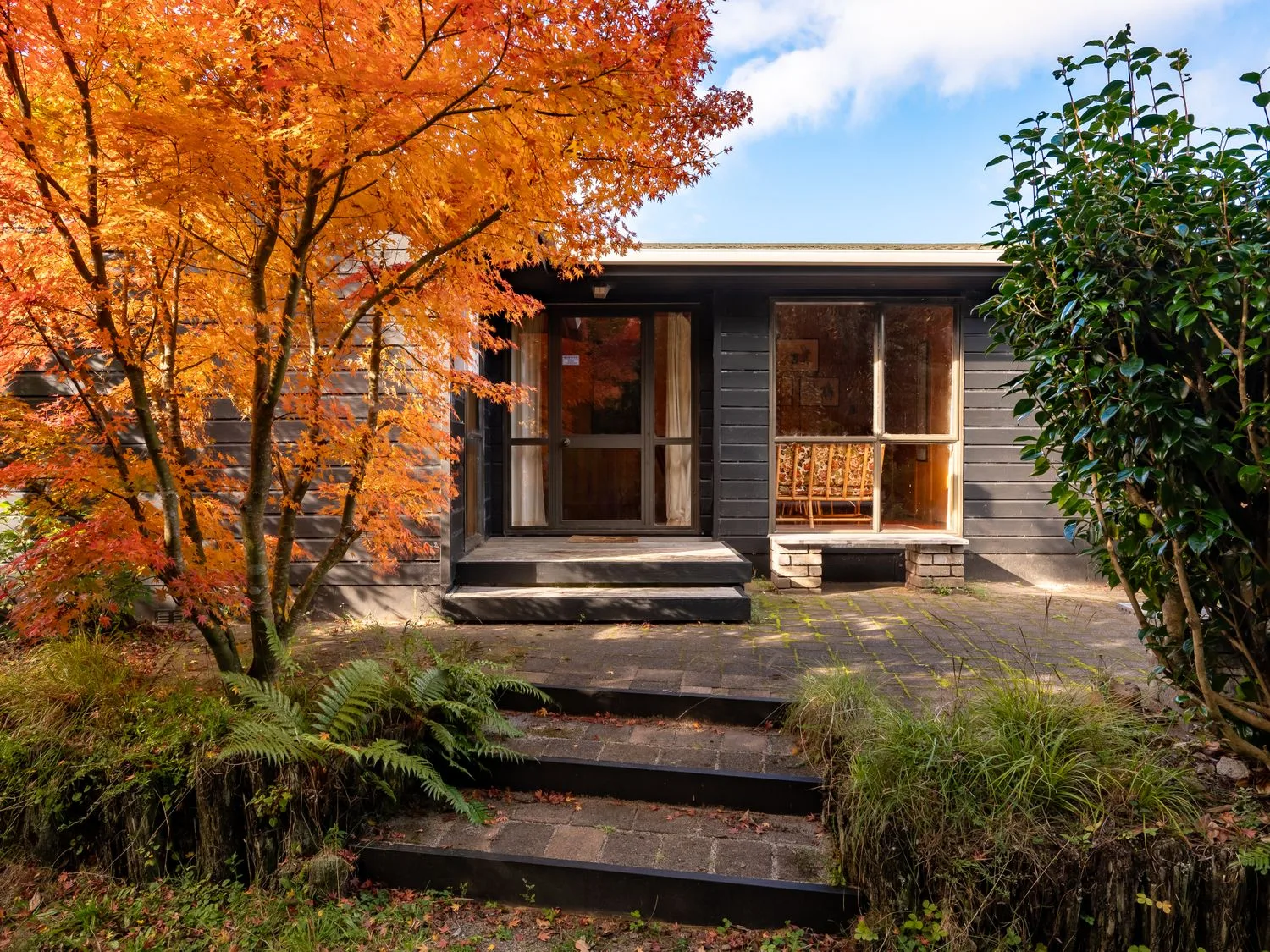 A house entrance with a glass door and window surrounded by autumn trees and plants at Lake View Lodge - Taupo Holiday Home in Pukawa Bay