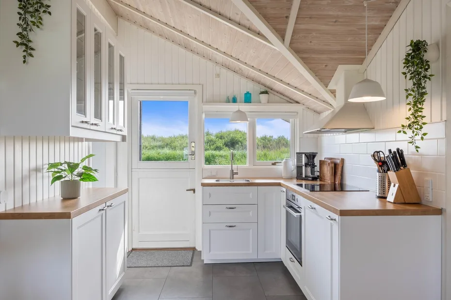 Una cocina luminosa con gabinetes blancos, encimeras de madera y una ventana con vistas a la vegetación.