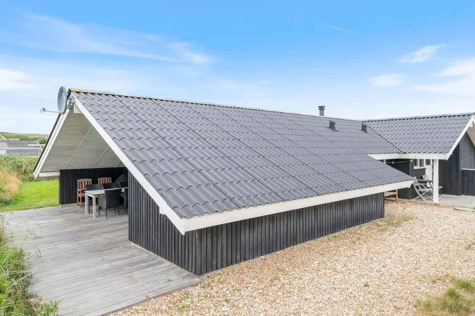 Una construcción de revestimiento oscuro y amplio techo gris junto a una terraza de madera.