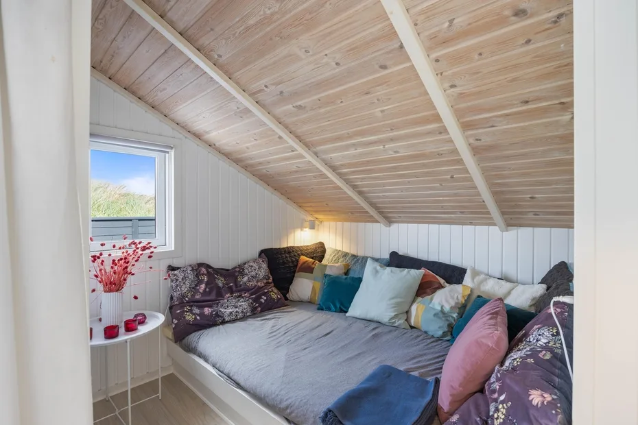 Un acogedor dormitorio con una cama baja llena de cojines de colores bajo un techo inclinado de madera.