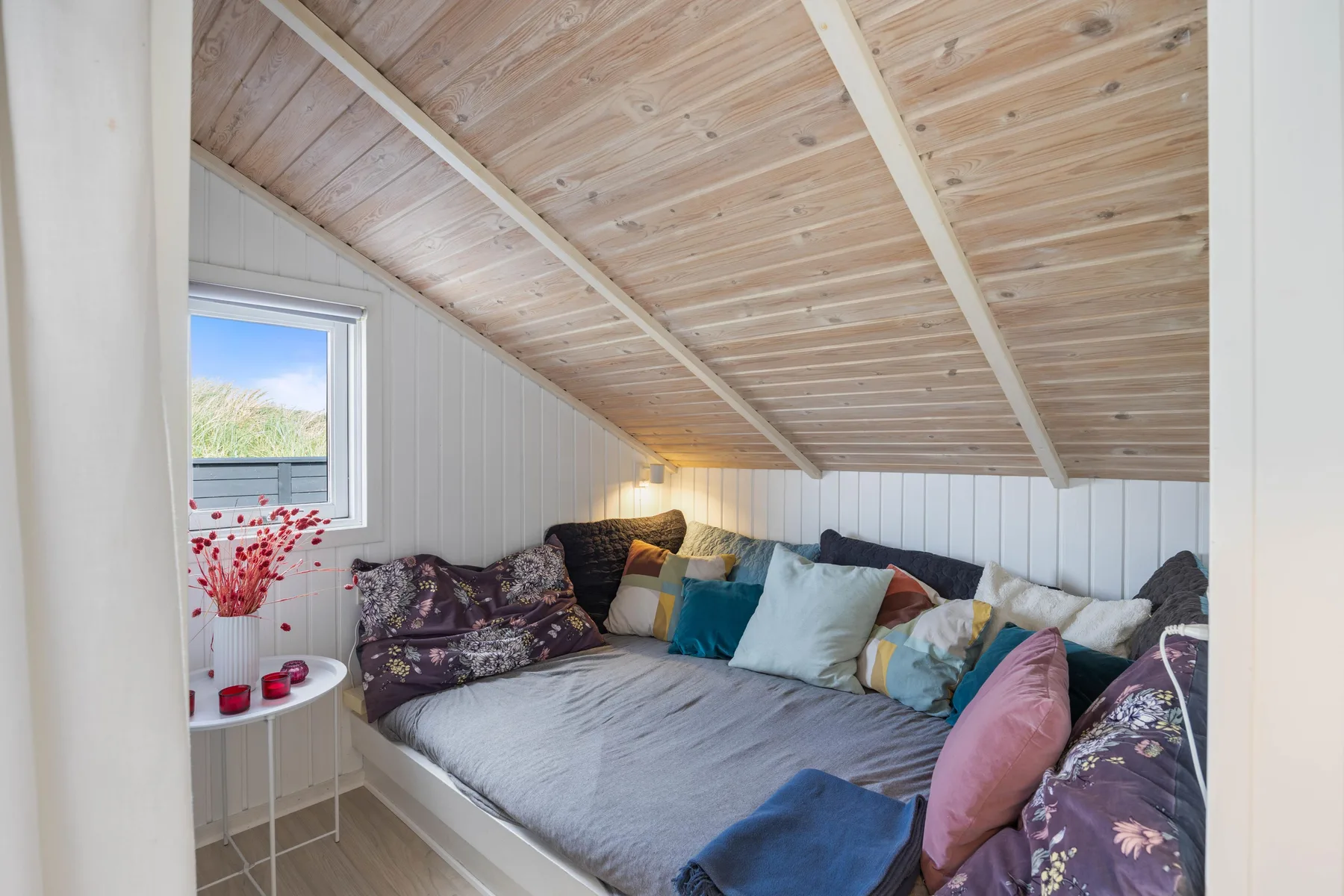 Un acogedor espacio para dormir bajo un techo inclinado de madera, con cojines de colores.