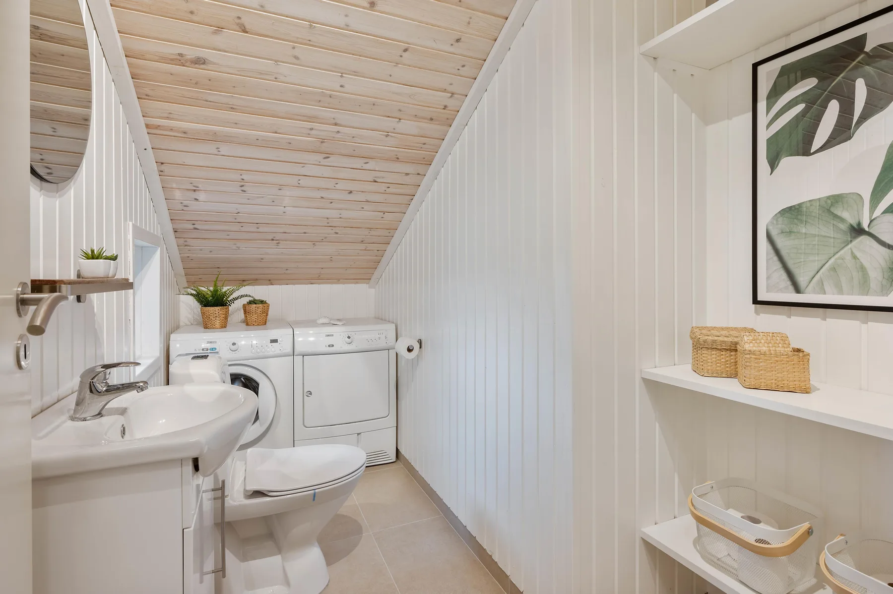 Un baño compacto con lavabo, inodoro y electrodomésticos de lavandería bajo un techo inclinado.