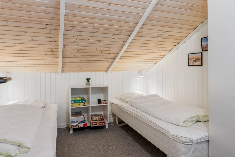 Un dormitorio abuhardillado y luminoso con dos camas y una pequeña estantería entre ellas.