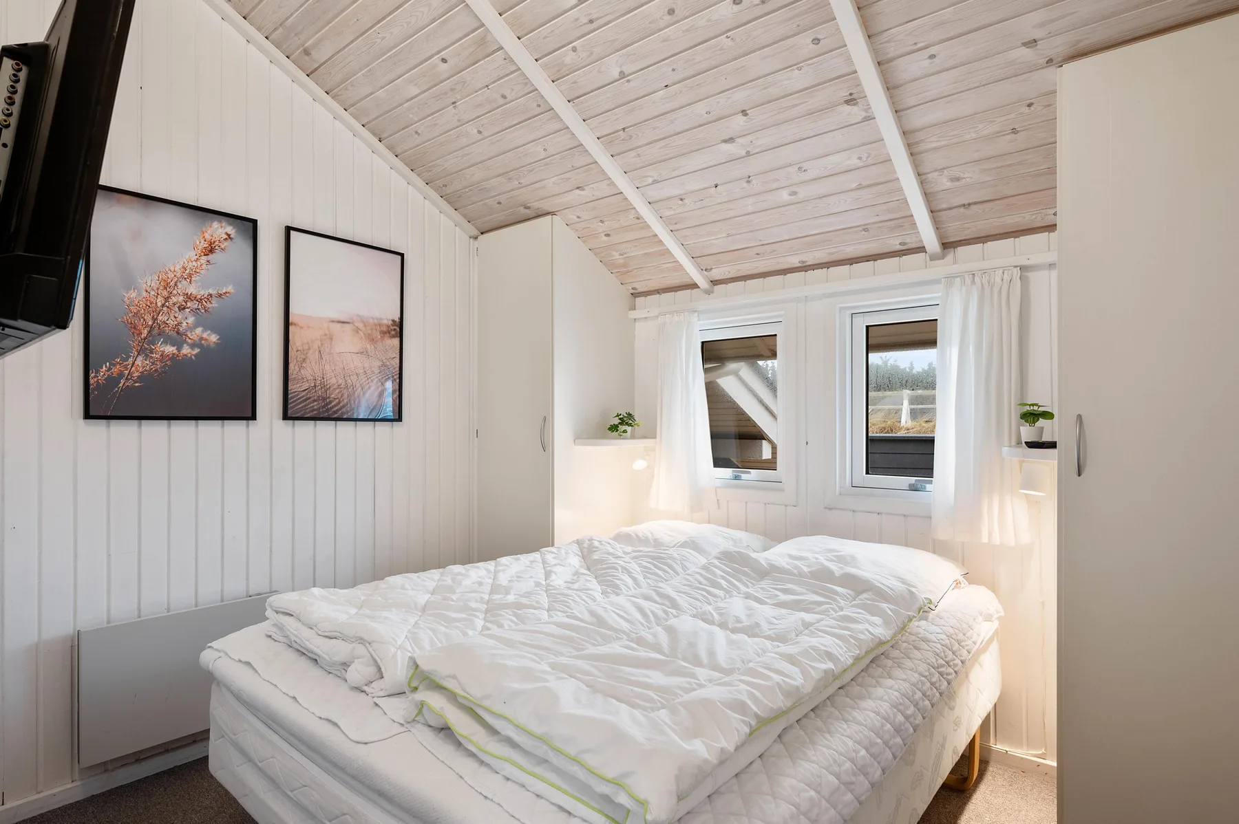 Un dormitorio luminoso con una cama bajo un techo inclinado de madera.