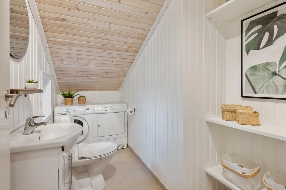 Un baño compacto con lavabo, inodoro y electrodomésticos de lavandería bajo un techo inclinado.