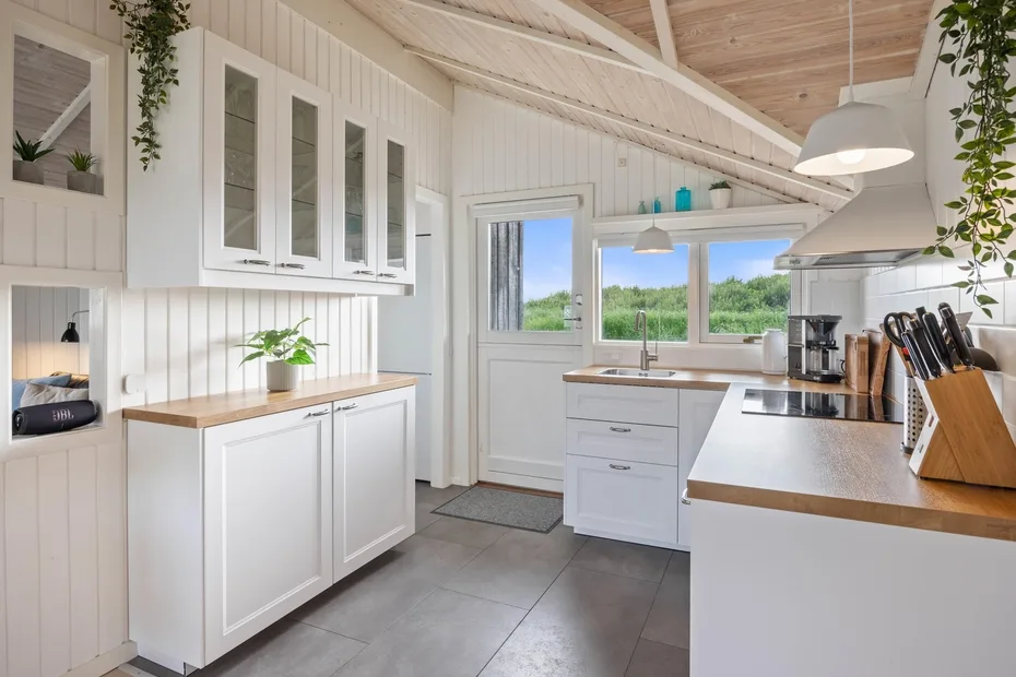 Una cocina luminosa con gabinetes blancos, encimeras de madera y ventanas con vistas a la vegetación.