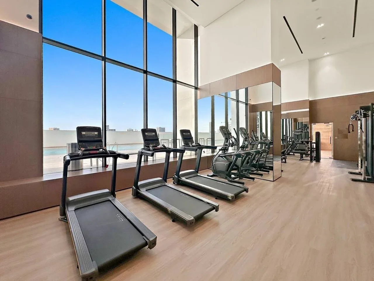 Un gimnasio con cintas de correr y equipo de ejercicio junto a ventanales.