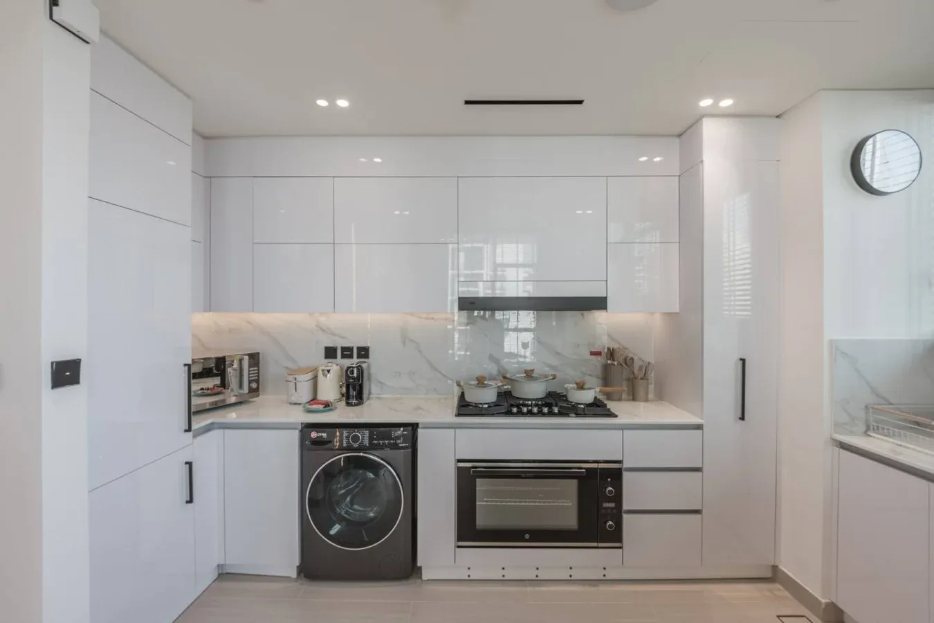 Una cocina blanca y luminosa con armarios, una placa de cocción y electrodomésticos integrados.