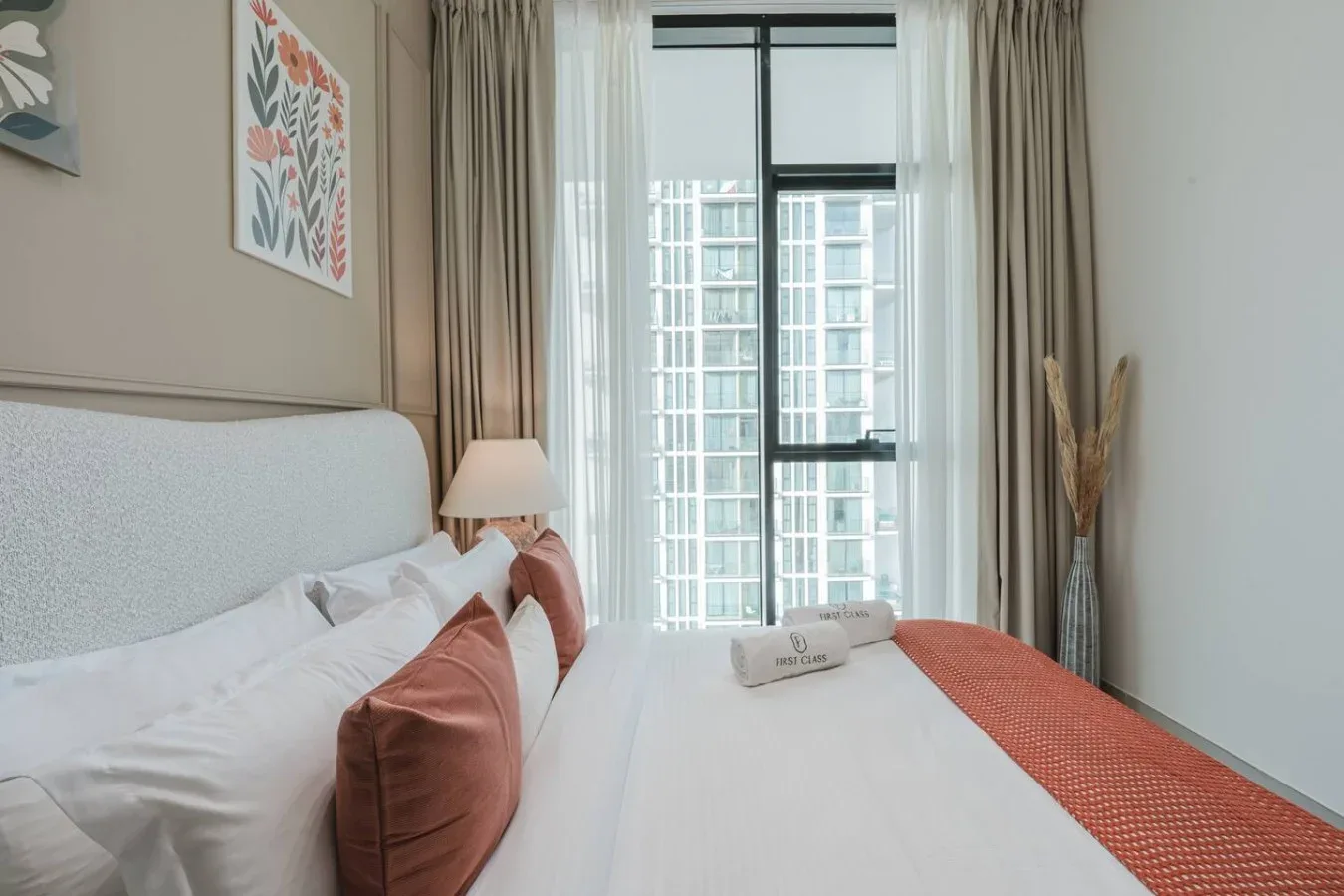 Un dormitorio luminoso con una cama tendida y ventanas altas con cortinas.