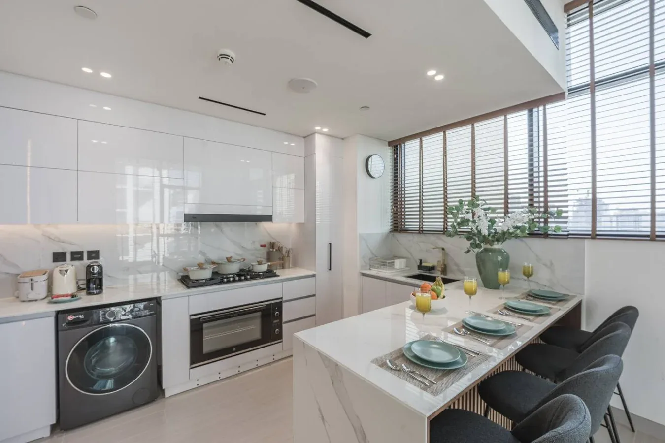 Una cocina moderna y luminosa con una mesa larga junto a grandes ventanas.