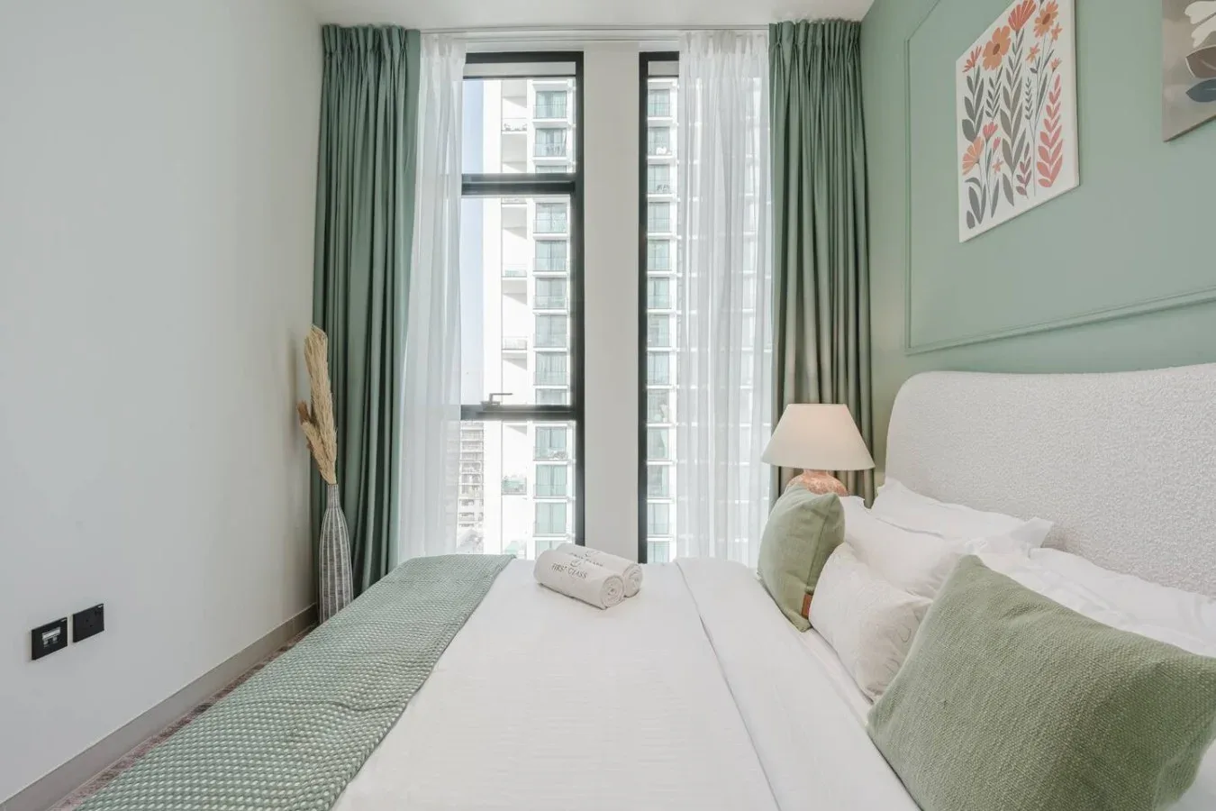 Dormitorio con una cama blanca, cortinas verdes y ventanas altas.