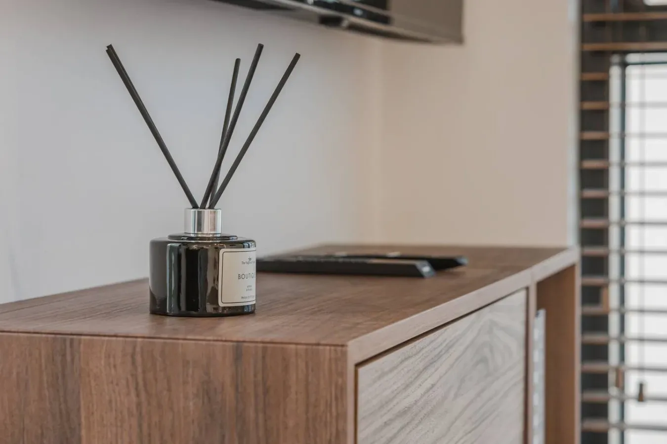 Un difusor de varillas está sobre un mueble de madera junto a una ventana.
