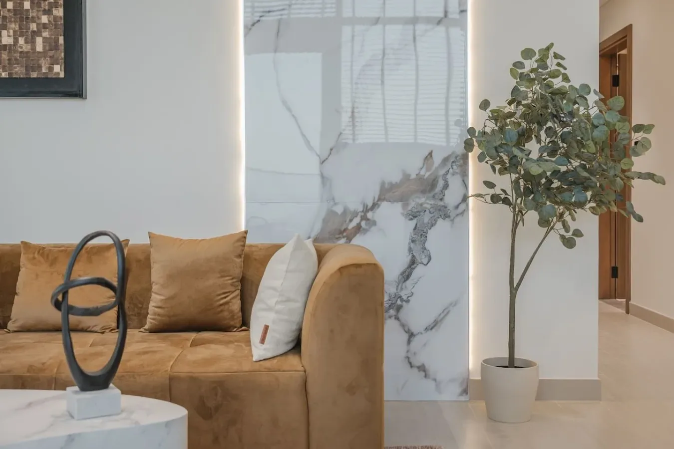 Una sala de estar con un sofá color canela, una planta en maceta y un panel de pared con vetas de mármol.
