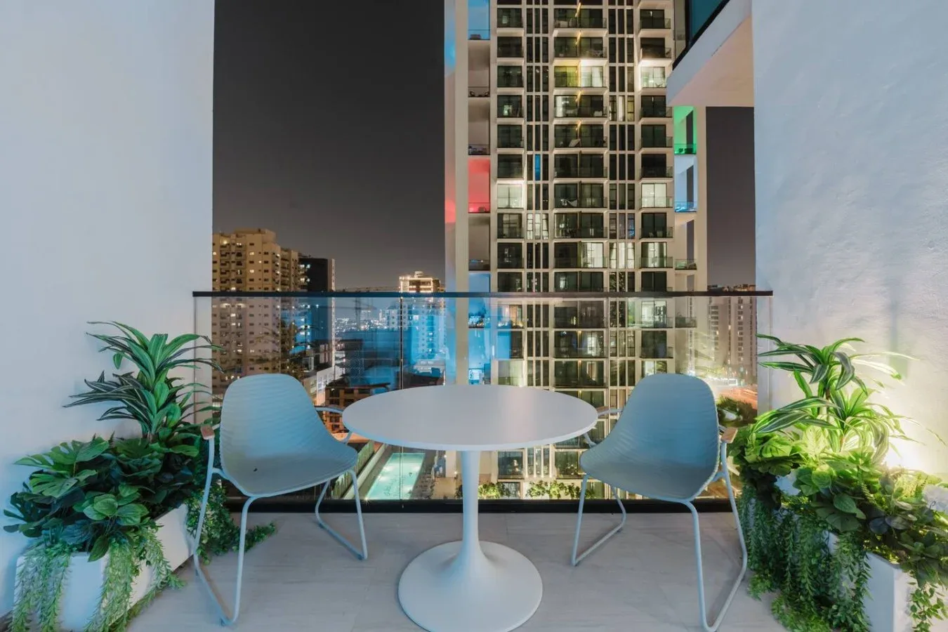 Una zona de estar en el balcón con una mesa redonda y vistas de la ciudad de noche.