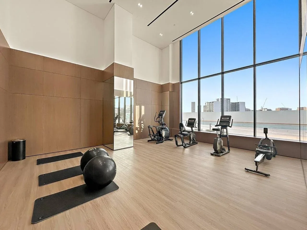 Un gimnasio luminoso con bicicletas estáticas, cintas de correr y colchonetas junto a grandes ventanales.