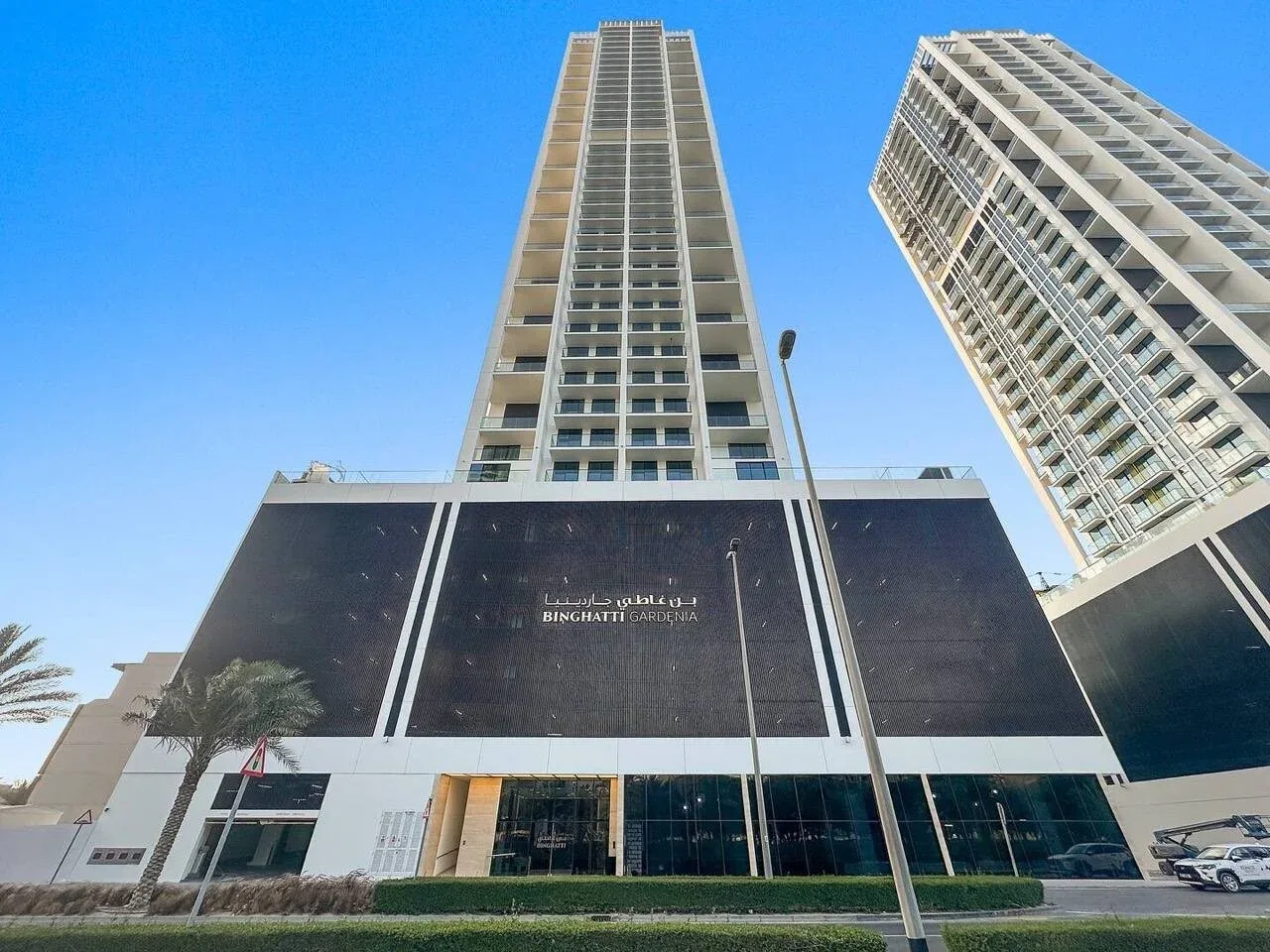 Dos torres modernas y altas se elevan sobre un edificio de paneles oscuros bajo un cielo azul despejado.
