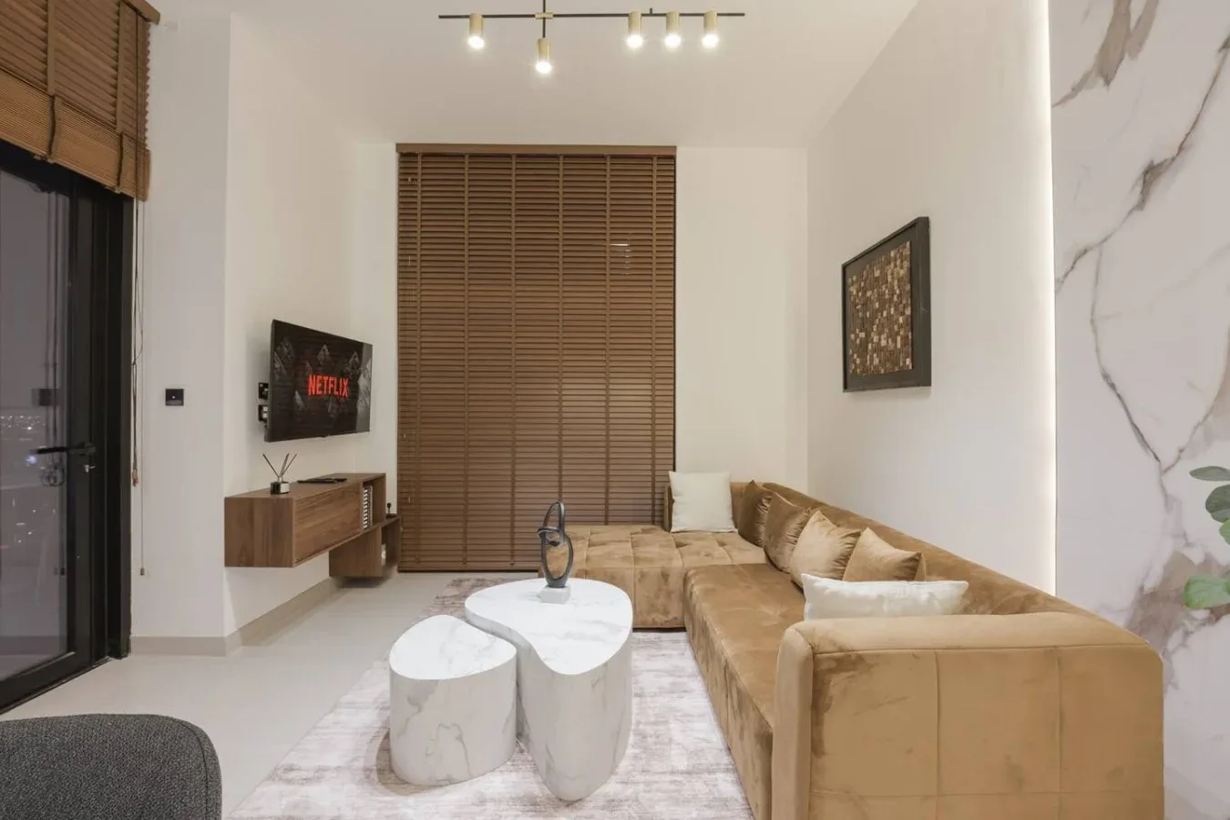 Una sala moderna con un sofá seccional color tostado y dos mesas de centro blancas.