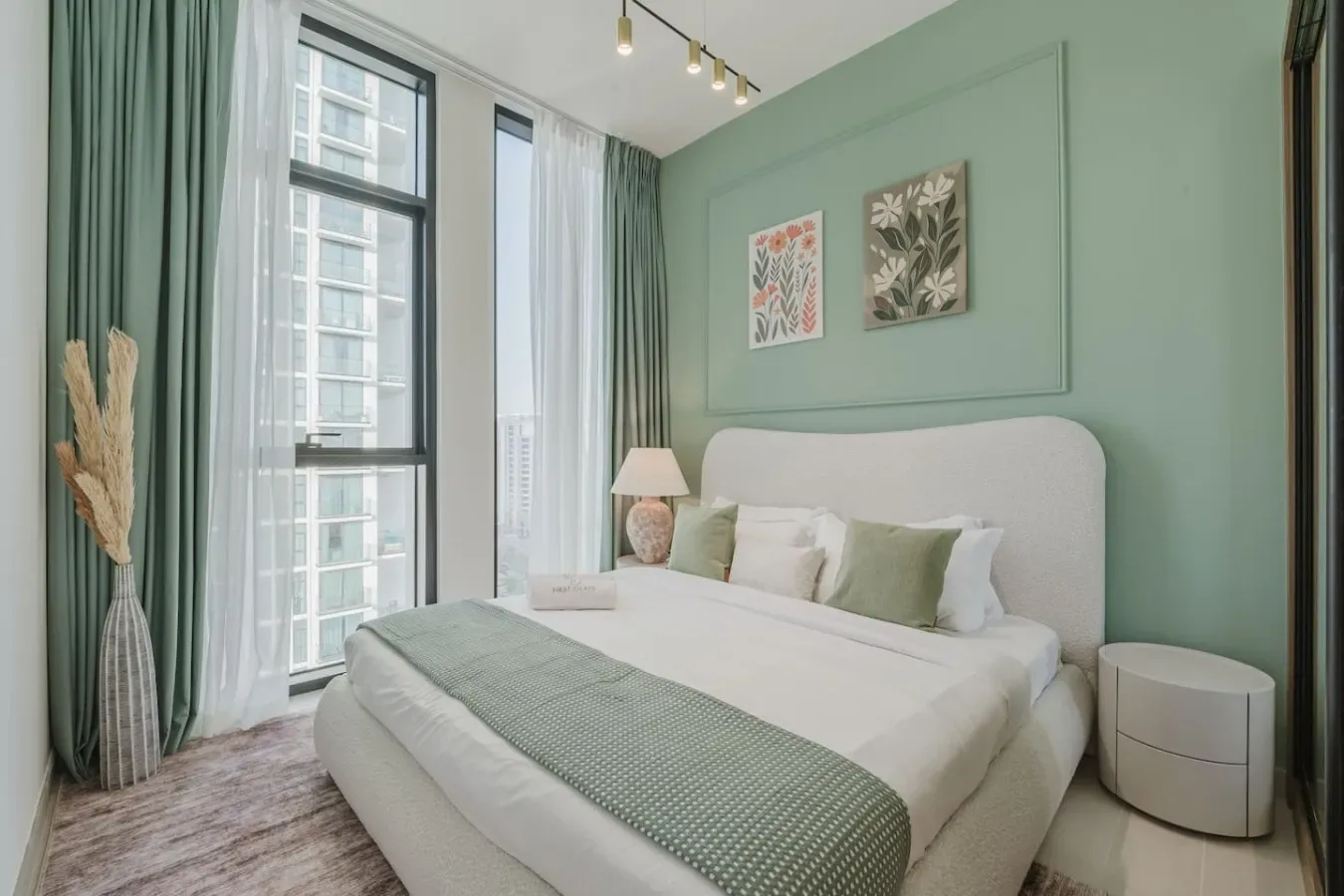 A bedroom with a bed, muted green accents, and tall windows.