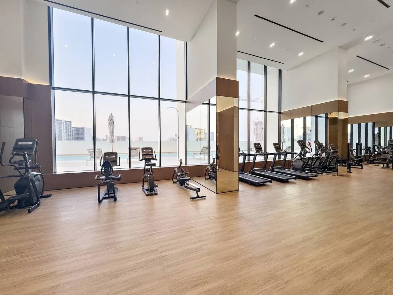 Un gimnasio luminoso con bicicletas estáticas y cintas de correr junto a grandes ventanales.