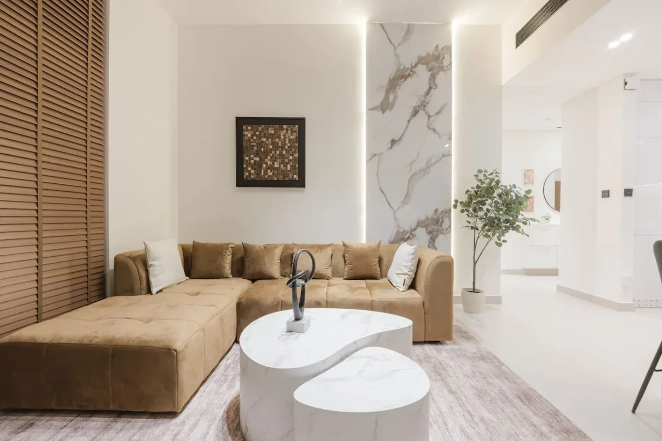 Una sala luminosa con un sofá seccional color tostado y dos mesas de centro blancas.