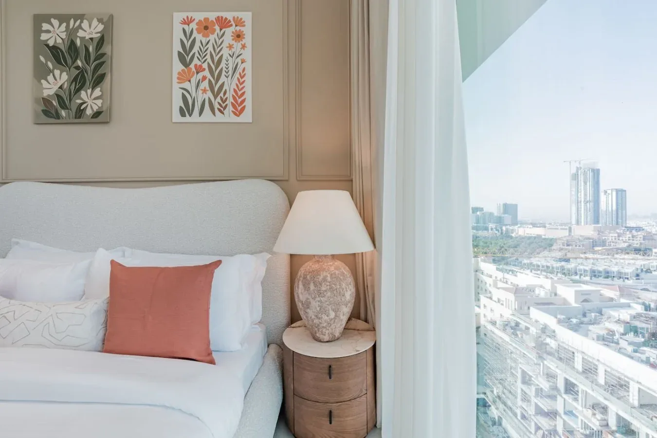 Un dormitorio con una cama bien tendida, una mesita de noche y vistas de la ciudad por la ventana.