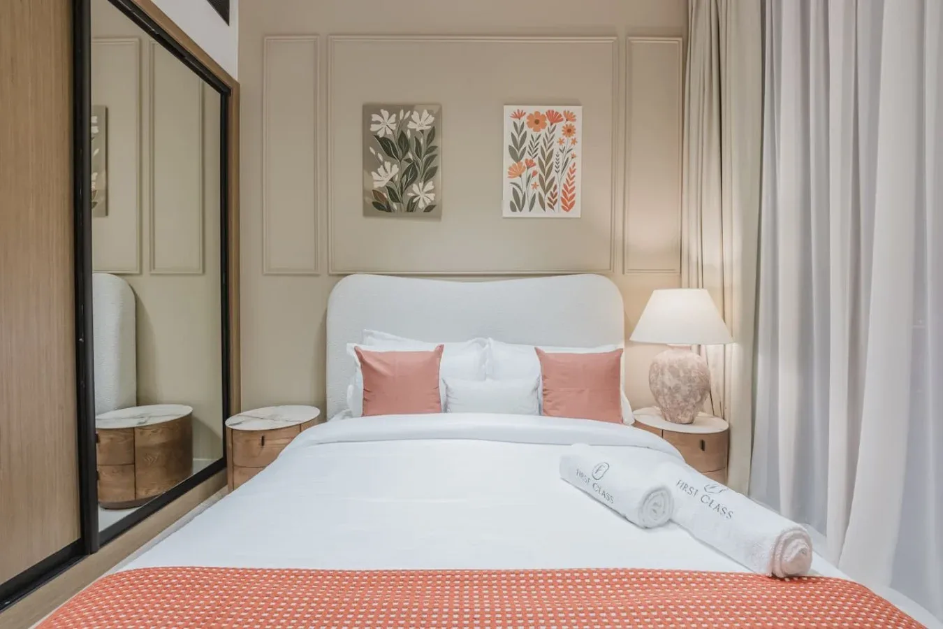 Un dormitorio con una cama tendida, cojines decorativos y láminas botánicas enmarcadas.