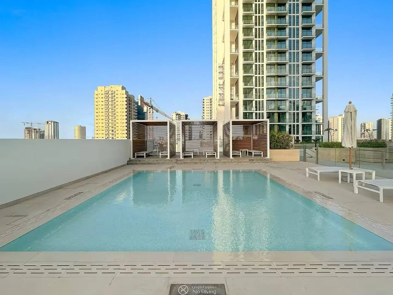 Una piscina en la azotea con asientos y edificios altos al fondo.