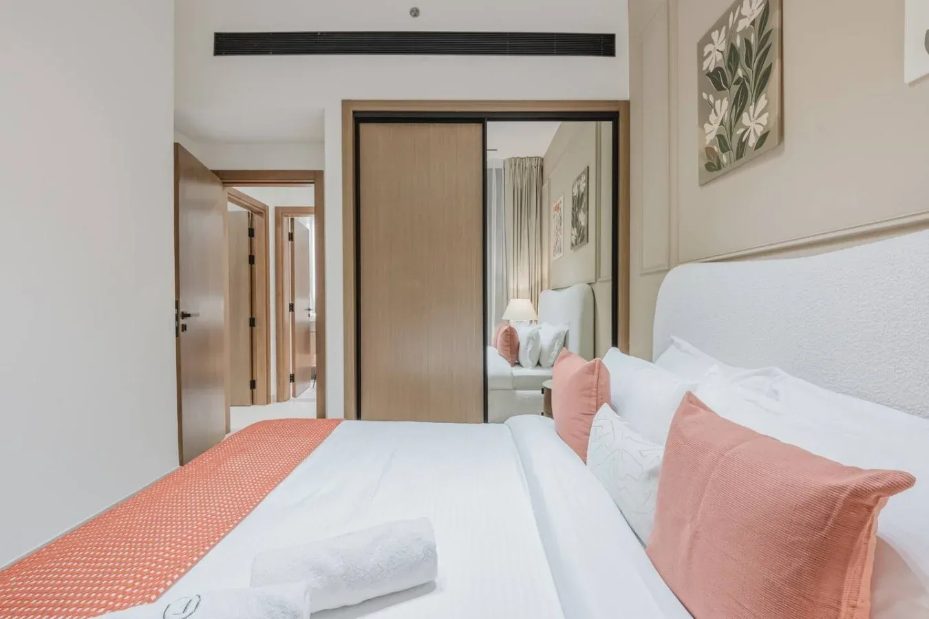 Un dormitorio con ropa de cama blanca y almohadas de color coral.