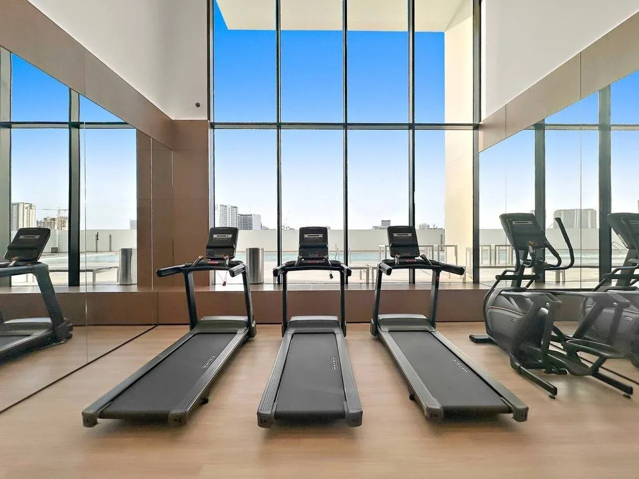 Un gimnasio con cintas de correr y equipos de ejercicio junto a ventanales.